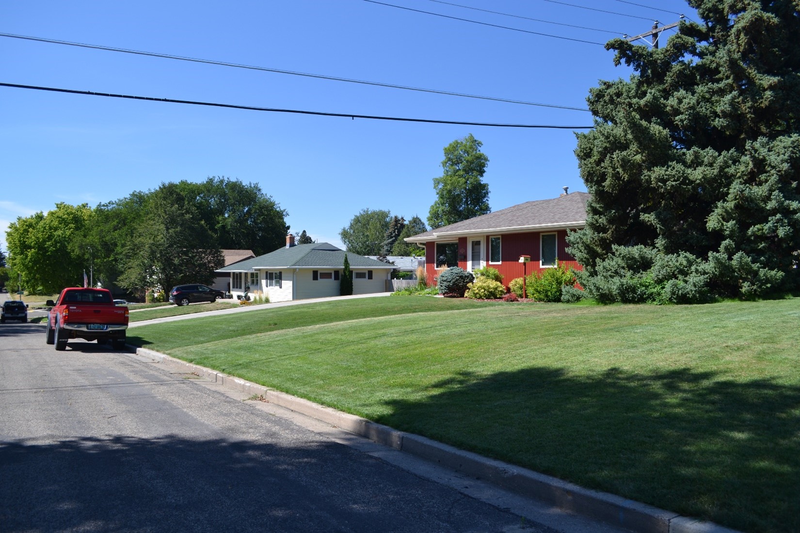 Street view of a red house with brown roof and white house with gray roof. A red pickup sits on the street, and a dark colored suv sits in the driveway in front of the white house.