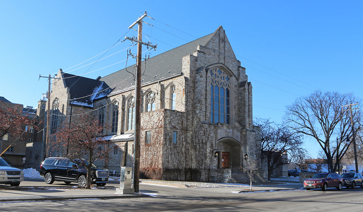 A brick or stone church with many beautiful windows and red or wood colored doors to the entrance.