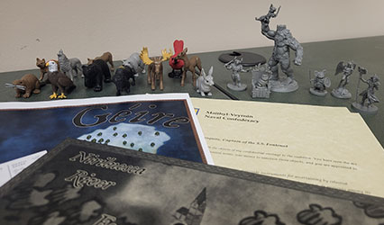 Figurines of animals and monsters stand on a table behind a few sheets of paper.