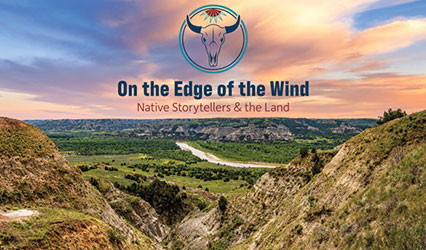 Outdoor scenery with buttes in the foreground, a river and greenery in the middleground, and more buttes in the background