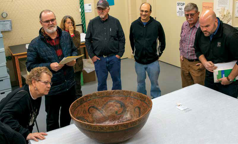A group of adults stand around a wooden bown with Norwegien writing on the inside