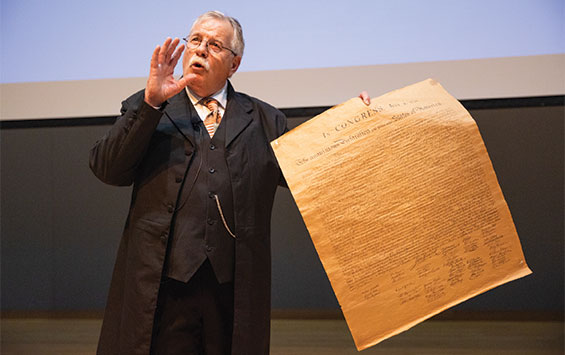 A man dressed as Theodore Roosevelt holds a large piece of paper